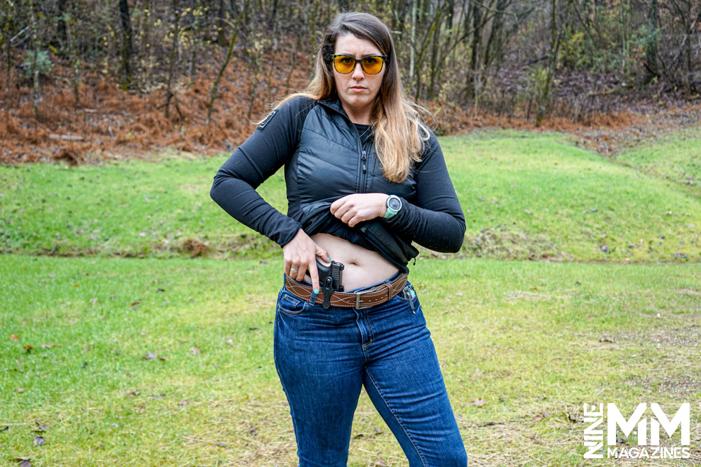 a photo of a woman drawing a gun from a hlster at a gun range