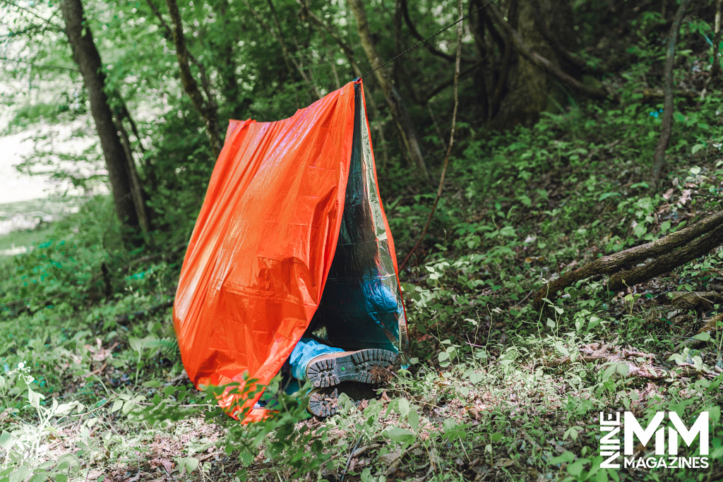 a photo of a man using a survival tent in the woods