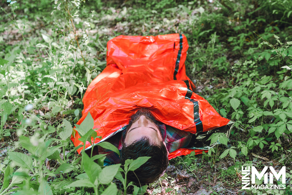 a photo of a man using an emergency sleeping bag in the woods