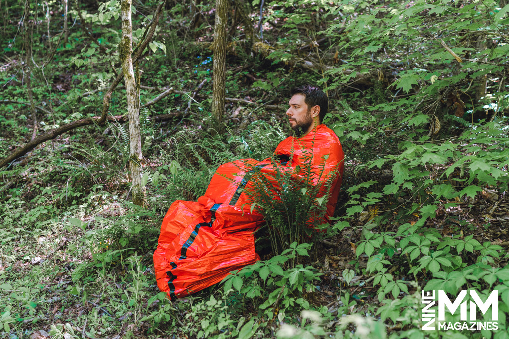 a photo of a man using an emergency live bivy in the woods